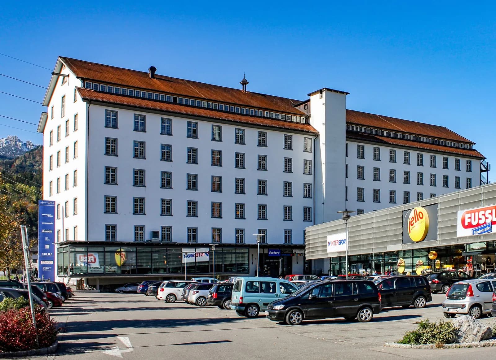 Lünersee Fabrik in Bürs bei Tag mit großem Parkplatz und angrenzendem Einkaufszentrum